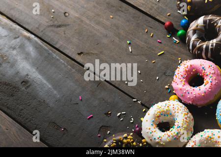 High angle view of fresh multi colored donuts with sprinklers and candies on wooden table Stock Photo