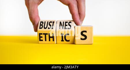 Business ethics symbol. Concept words Business ethics on wooden blocks. Businessman hand change words business on ethics. Beautiful yellow table white Stock Photo