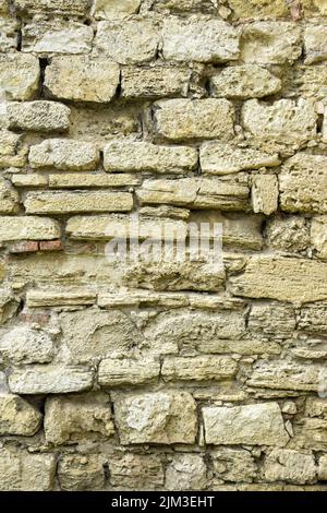 Masonry wall of old stone blocks of limestone. Background texture of ancient brick wall. Full frame. Vertical photo. Selective focus. Stock Photo