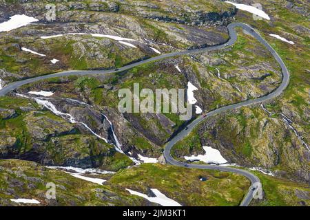 Winding road in a green landscape with snow patches seen in Norway Stock Photo