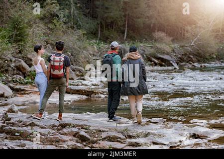 Back view on two couples at rocky fast mountains river standing hand in hand and enjoying view. Stock Photo