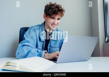 A smiling young man working on his laptop in the office or at home Stock Photo