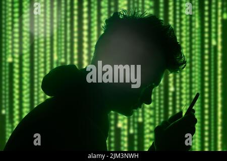 A man in a hoodie watching on his phone as a hacker concept Stock Photo