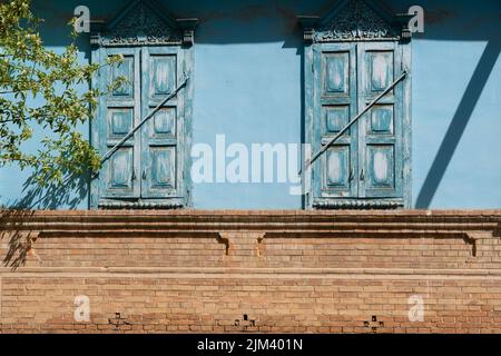 An old brick building with a blue-colored wall and wooden shutters Stock Photo