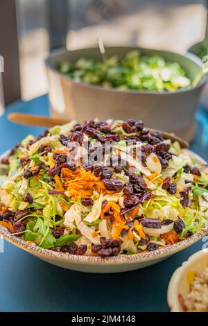 Arugula salad, lettuce, red cabbage, carrots and dried cranberries in a bowl with other salads and dishes around it. Stock Photo
