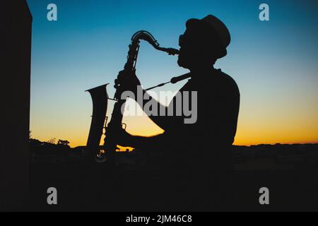 A silhouette of a man playing saxophone during sunset Stock Photo