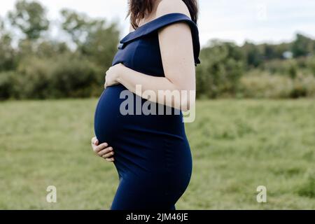 A young 38 weeks pregnant woman in a blue dress holding her belly Stock Photo