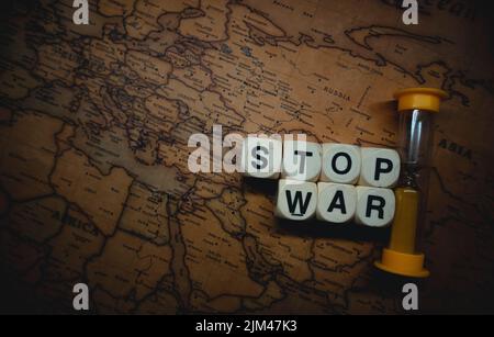 A closeup of an hourglass and cube words "stop war" placed between Russia and Ukraine on a world map Stock Photo