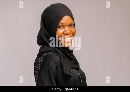 An African Muslim woman with a happy smile in a black outfit isolated over gray background Stock Photo