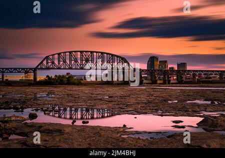 A beautiful scene of the Big Four Bridge in Louisville, Kentucky reflecting on wet land against a cloudy colorful sky Stock Photo