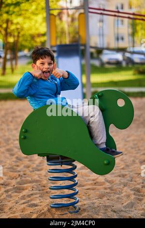 A child sitting on fish-shaped wooden swing equipment at a playground in the Stare Zegrze district. Stock Photo