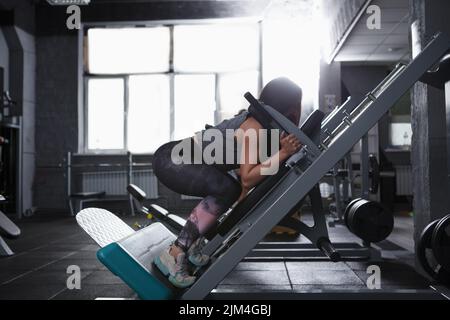 Profile shot of a strong athletic woman doing squats in hack squat gym machine Stock Photo