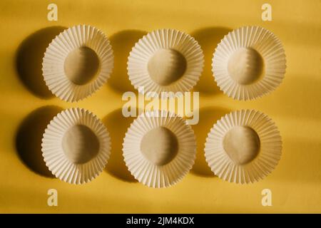 empty baking paper cups. white cookie paper cases isolated on yellow background with shadow Stock Photo