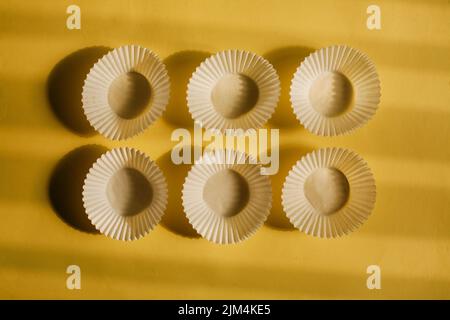 empty baking paper cups. white cookie paper cases isolated on yellow background with shadow Stock Photo