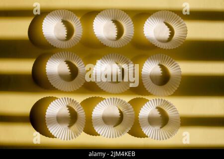 empty baking paper cups. white cookie paper cases isolated on yellow background with shadow Stock Photo