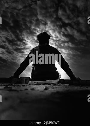 A vertical shot of a silhouette of a lonely young man looking at the horizon. Stock Photo