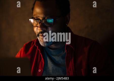 Black bearded man in eyeglasses working with laptop indoors Stock Photo