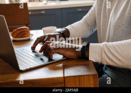 Black man working with laptop while having breakfast at home Stock Photo