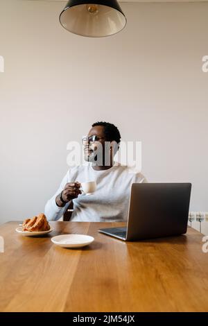 Black man working with laptop while having breakfast at home Stock Photo