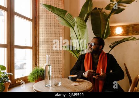 Black man using cellphone while drinking coffee in cafe indoors Stock Photo