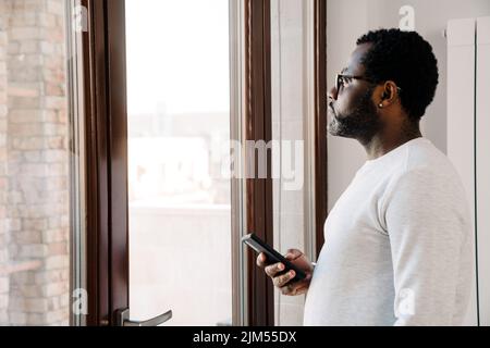 Black bearded man wearing eyeglasses looking in window at home Stock Photo