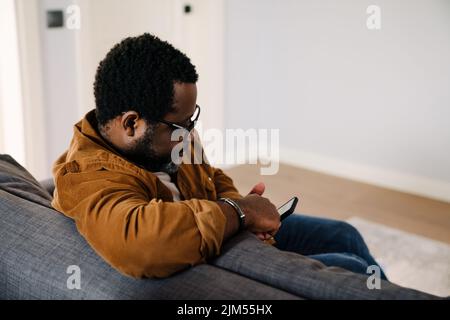 Black bearded man using cellphone while sitting on sofa at home Stock Photo