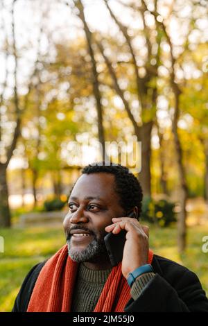 Black bearded man talking on cellphone while strolling at park Stock Photo