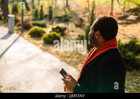 Black bearded man using cellphone while strolling in park Stock Photo
