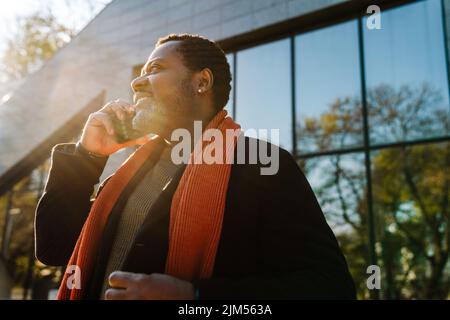Black bearded man smiling and talking on cellphone at city street Stock Photo