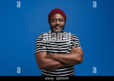 Black bearded man wearing hat smiling and looking at camera isolated over blue background Stock Photo
