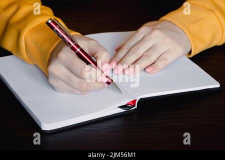 Woman writing in blank notebook. Close-up of hand holding pen. Businesswoman takes notes in office. Stock Photo