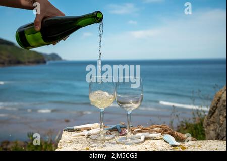 Pouring of txakoli or chacolí slightly sparkling very dry white wine produced in Spanish Basque Country, served outdoor with view on Bay of Biscay, At Stock Photo