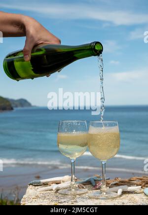 Pouring of txakoli or chacolí slightly sparkling very dry white wine produced in Spanish Basque Country, served outdoor with view on Bay of Biscay, At Stock Photo