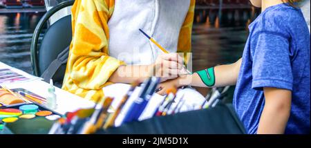 Young girl artist draws a dragon on child's hand. Process of drawing on skin, close-up, banner. Stock Photo