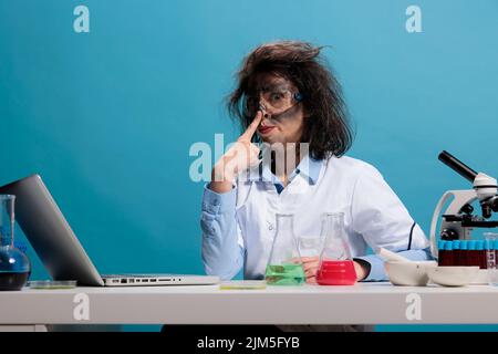 Portrait of crazy amusing chemist acting funny and having dirty face and messy hair while sitting at desk and looking at camera. Mad scientist with wild appearance acting silly after lab explosion Stock Photo