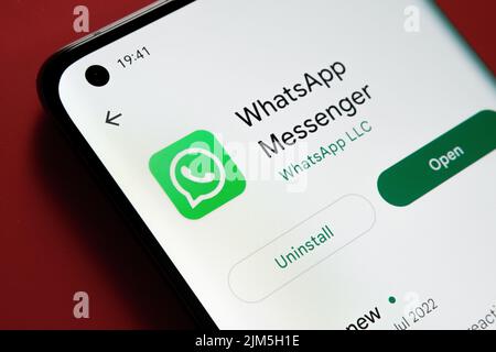 WhatsApp app seen in Google Play Store on the smartphone screen placed on red background. Close up photo with selective focus. Stafford, United Kingdo Stock Photo