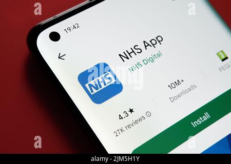 NHS app seen in Google Play Store on the smartphone screen placed on red background. Close up photo with selective focus. Stafford, United Kingdom, Au Stock Photo