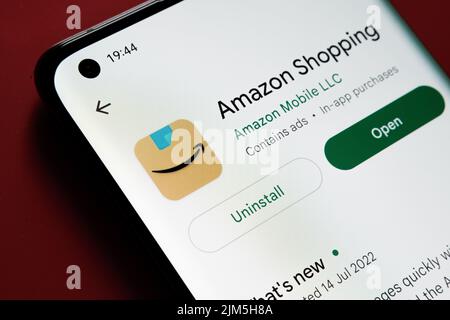 Amazon Shopping app seen in Google Play Store on the smartphone screen placed on red background. Close up photo with selective focus. Stafford, United Stock Photo