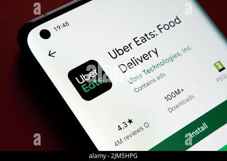 uber eats app seen in Google Play Store on the smartphone screen placed on red background. Close up photo with selective focus. Stafford, United Kingd Stock Photo