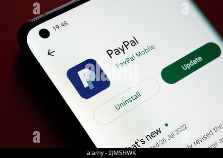 PayPal app seen in Google Play Store on the smartphone screen placed on red background. Close up photo with selective focus. Stafford, United Kingdom, Stock Photo