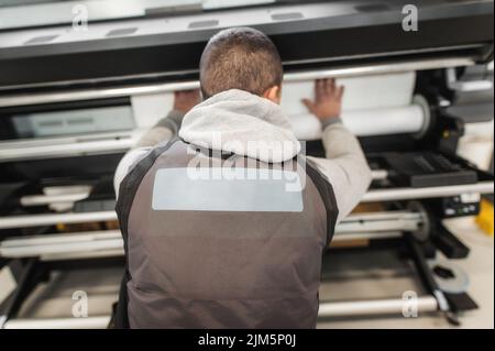 Technician worker operator changes the paper roll on large premium industrial printer and plotter machine in digital printshop office Stock Photo