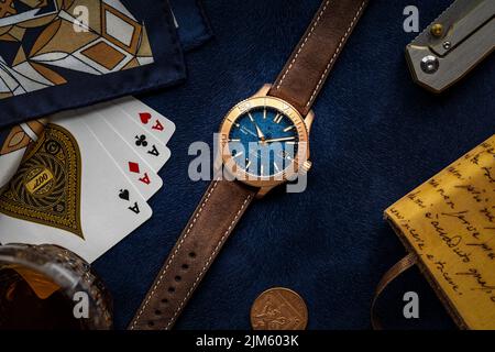 A top view of Christopher Ward C60 Trident Bronze Watch surrounded by playing cards on blue background Stock Photo