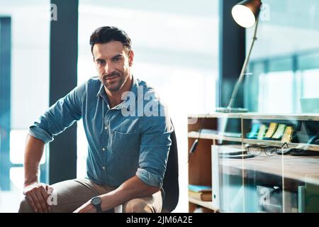 A confident, serious and powerful male entrepreneur sitting in a modern office or workplace. Portrait of a business man, leader or employer ready to Stock Photo