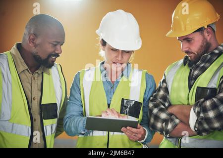 Construction projects gone paperless. a group of builders using a digital tablet while working at a construction site. Stock Photo