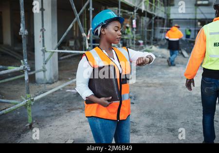 Time is the most important power tool on this site. a young woman checking the time while working at a construction site. Stock Photo
