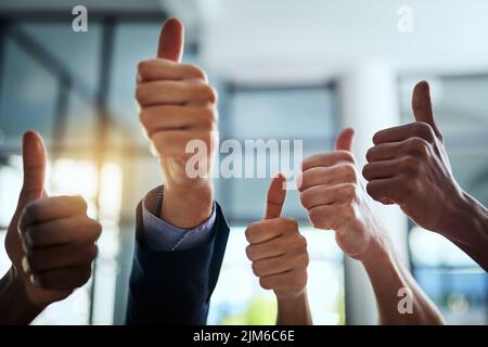 Thumbs up, support and hand sign shown by professional corporate business people in an office together. Employees and colleagues working and showing Stock Photo