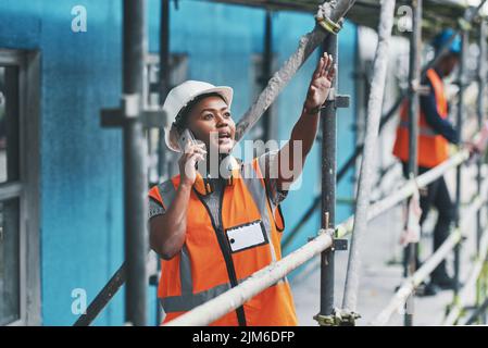 Springing into action as the supervisor. a young woman talking on a cellphone while working at a construction site. Stock Photo