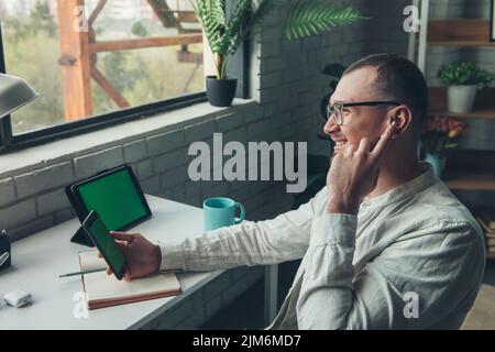 Smiling man sitting at desk talking on mobile phone writing in notebook. Mobile communication. Working remotely. Corporate business technology. Stock Photo
