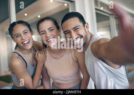 Gym selfies with friends. Cropped portrait of three young athletes taking selfies while standing in the gym. Stock Photo