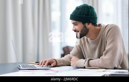 Staying home and still churning out awesome designs. a confident young man using a laptop while working from home. Stock Photo